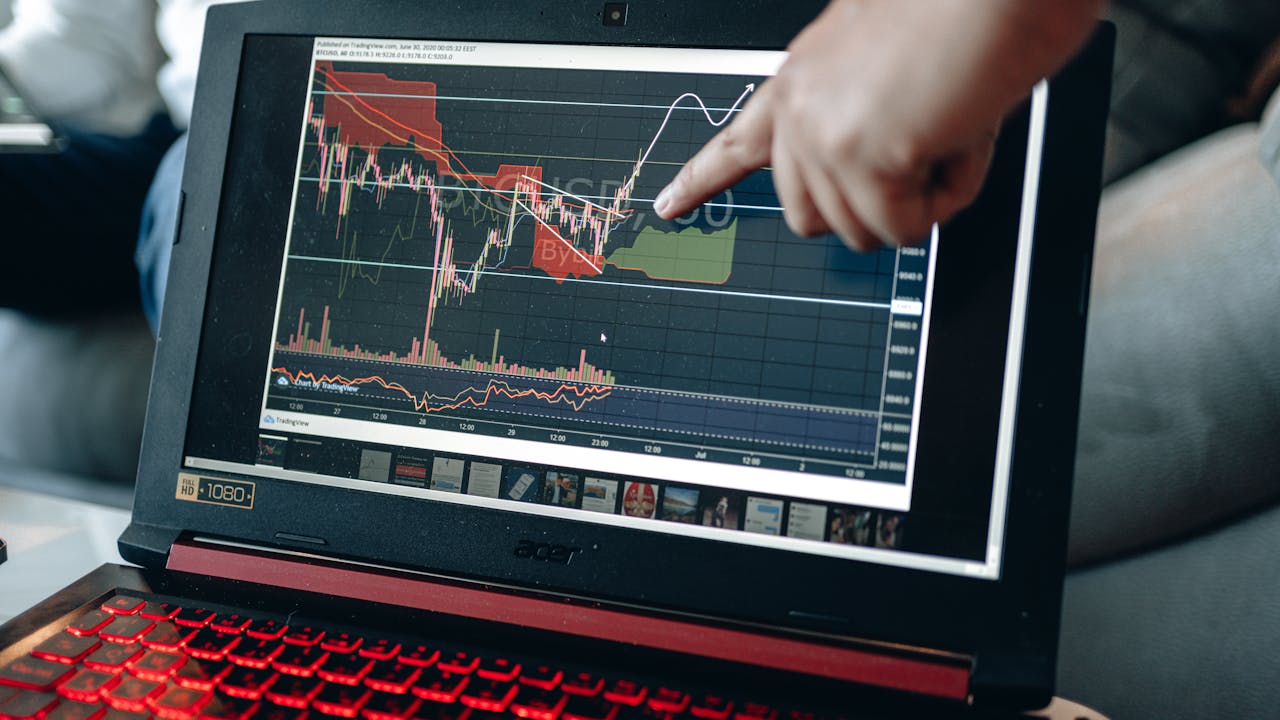 services-04 A person points at graph on laptop, analyzing stock trends for investment insights.